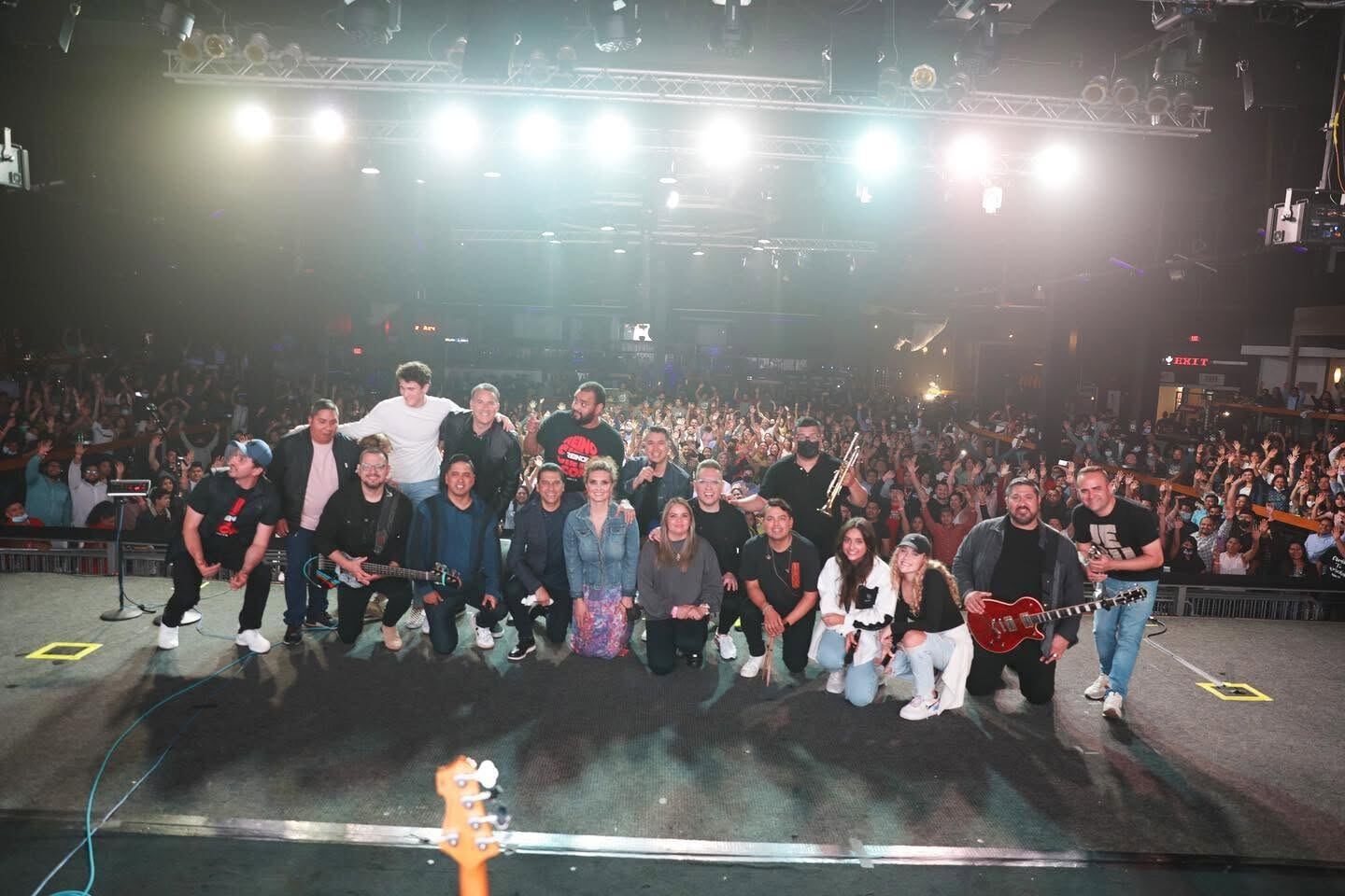 Foto de grupo en el escenario, con el público detrás y las luces de frente
