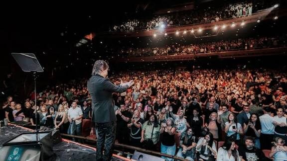 Un hombre en el escenario, frente a un teatro lleno con balcones