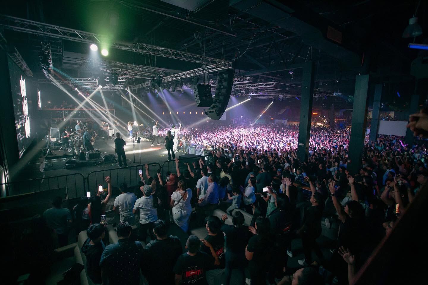 Recinto lleno, con haces de luz sobre la banda en el escenario
